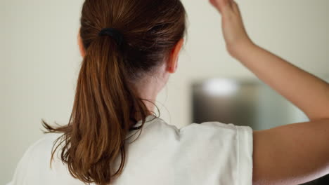 tired woman strokes head standing in room closeup. lady in white t-shirt adjusts hair wiping sweat on blurry background. exhausted woman at home