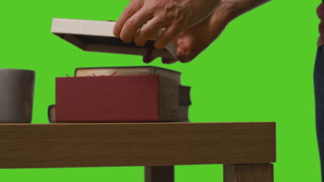 close up of man opening gift wrapped present on table shot against green screen