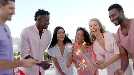 um grupo feliz e diversificado de amigos queimando faíscas em círculo na praia