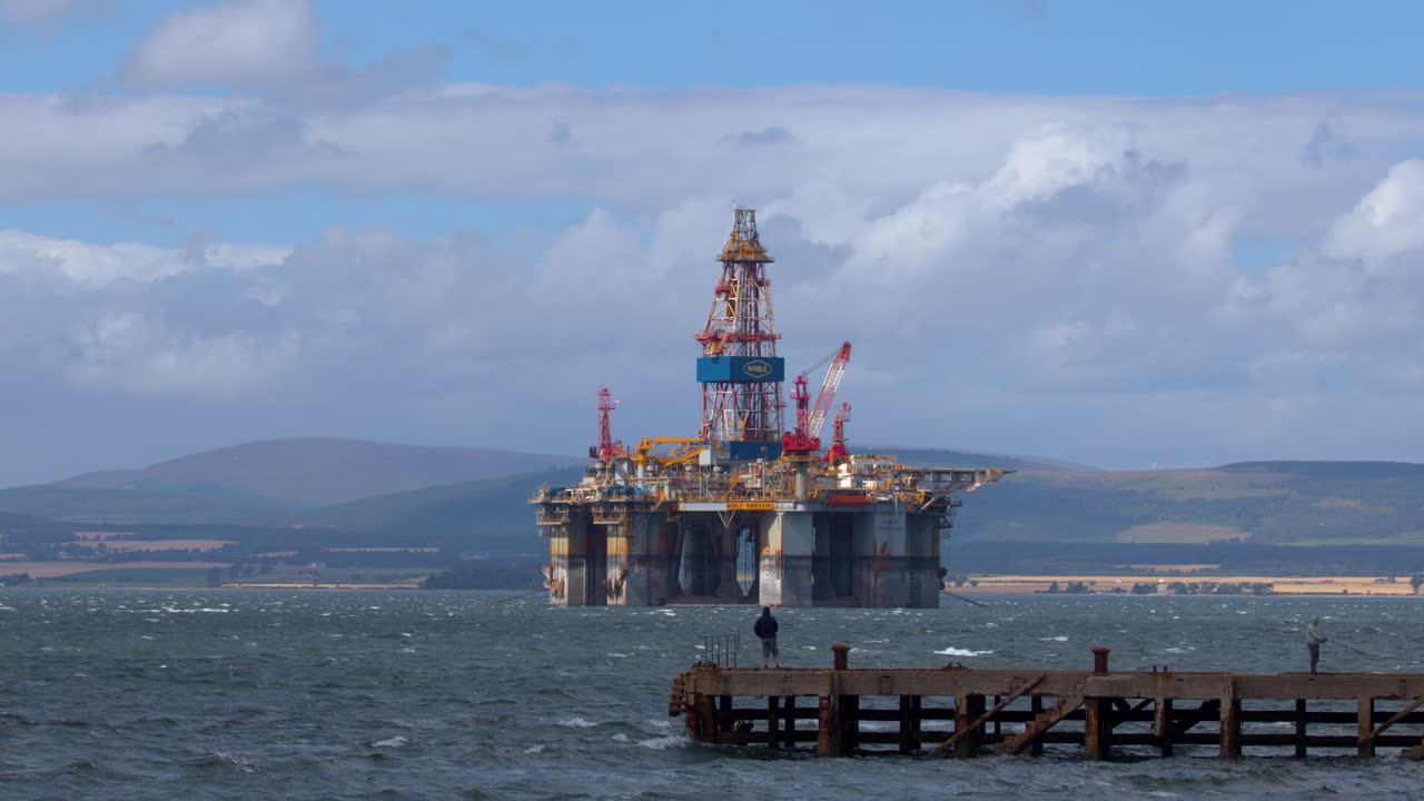 Oil drilling platform offshore, fisherman on pier, daylight, wide shot, Highlands landscape, steady camera