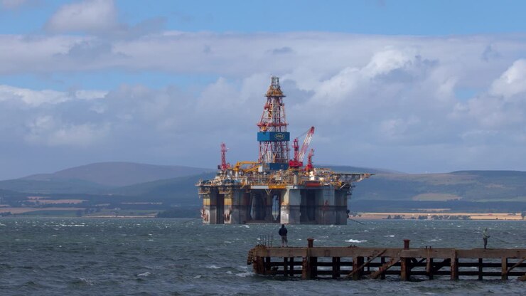 Oil drilling platform offshore, fisherman on pier, daylight, wide shot, Highlands landscape, steady camera
