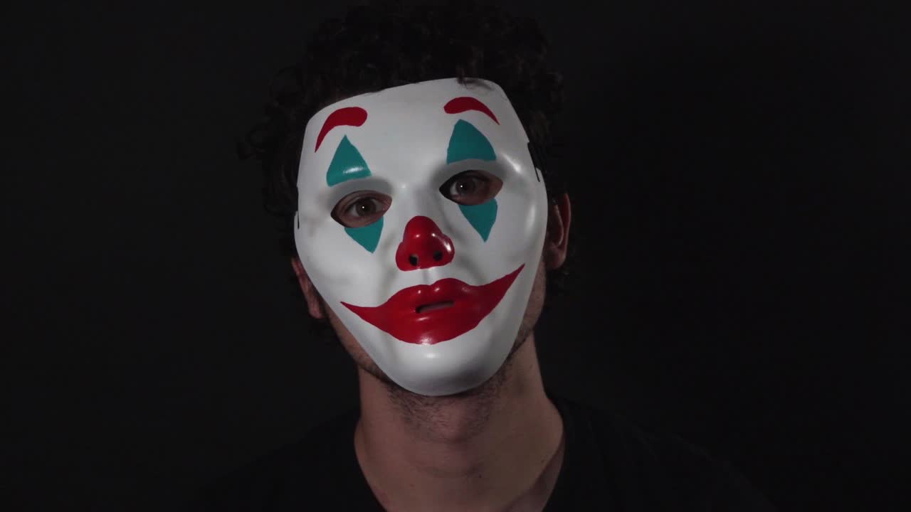 hombre que lleva la máscara de payaso con el tema del bromista en una habitación negra oscura