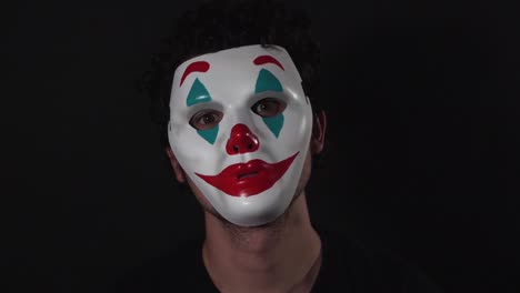 man wearing the joker themed clown mask in dark black room