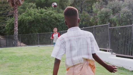 black pre-teen boy throwing a football to his hispanic friend in the park, slow motion