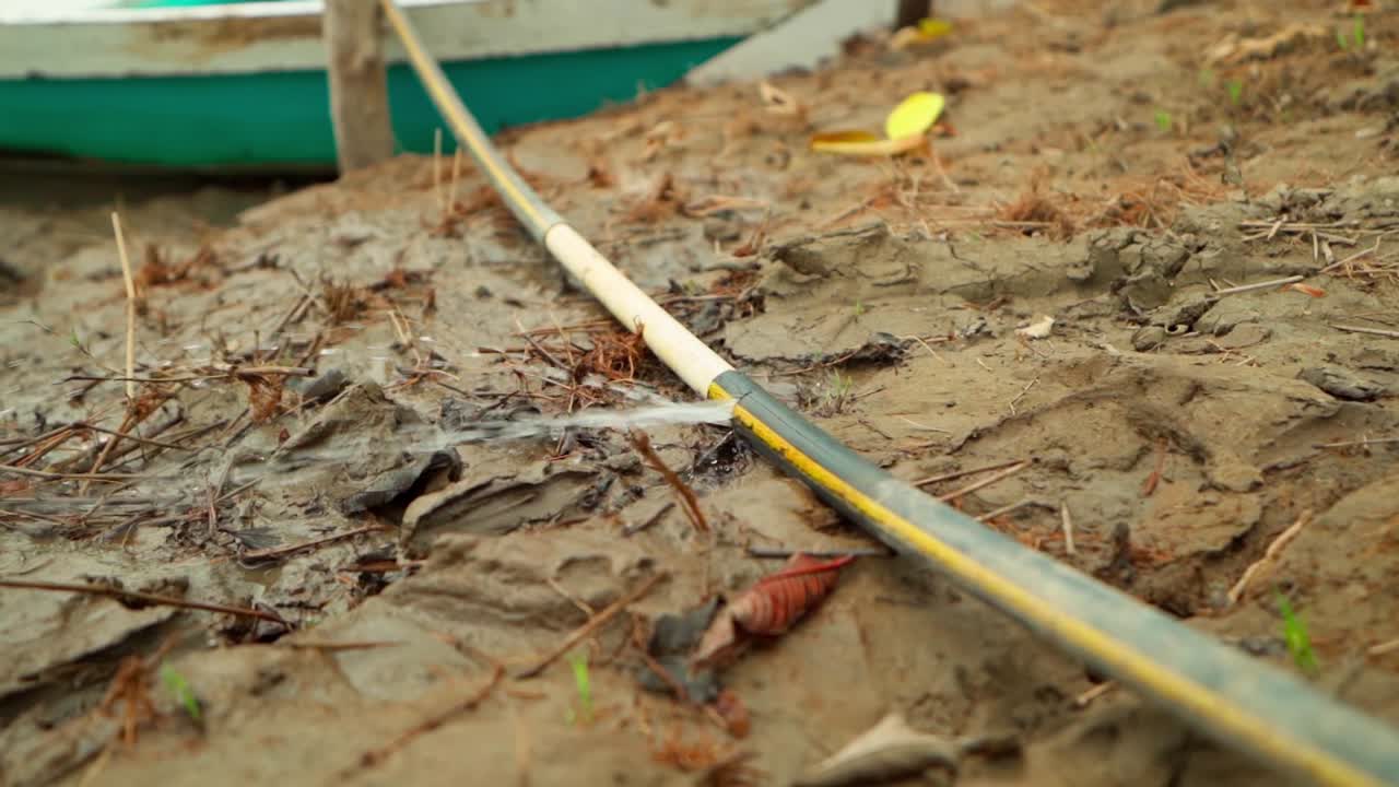 A water hose leaking onto the wet, sandy ground near leaves and debris