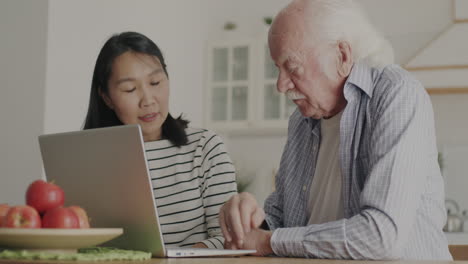 young woman helping elderly man use laptop