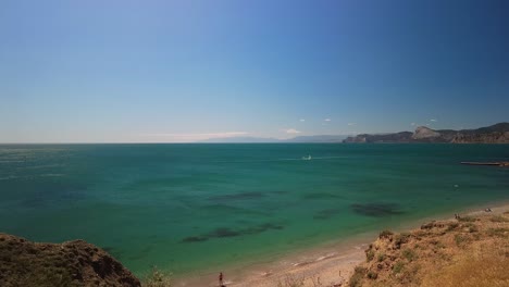 Crimea,-Cape-Megan,-surfers-with-a-sail-cut-through-the-green-water-of-the-Black-Sea