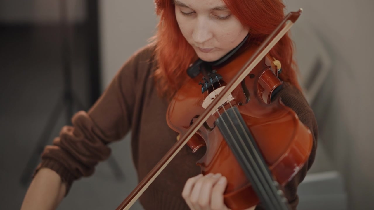 Rødhåret fiolinist øver. Kvinne med flammende hår konsentrerer seg om å spille fiolin under øving. Ung rødhåret musiker øver flittig på fiolinfremføringen sin i et klasseromsmiljø