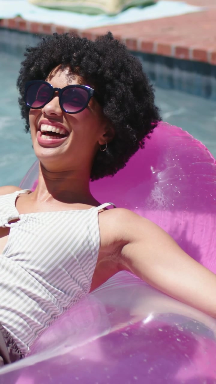 Vertical video: Cam zooming woman turning head laughing on pink float at pool, swim top and shades