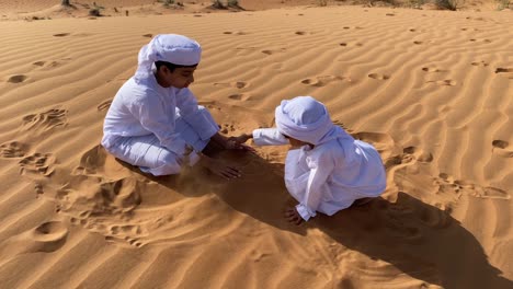 two emarati children playing with sand in the desert