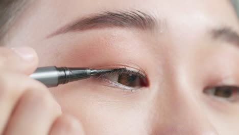 close up of beautiful young asian woman applying eyeliner doing perfect eye arrows and smiling while wearing makeup at home