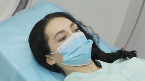 la paciente femenina con máscara se somete a una tomografía computarizada o resonancia magnética en una clínica médica moderna. la paciente está acostada en una mesa de escaneo computarizado o mri, entra en la máquina ino