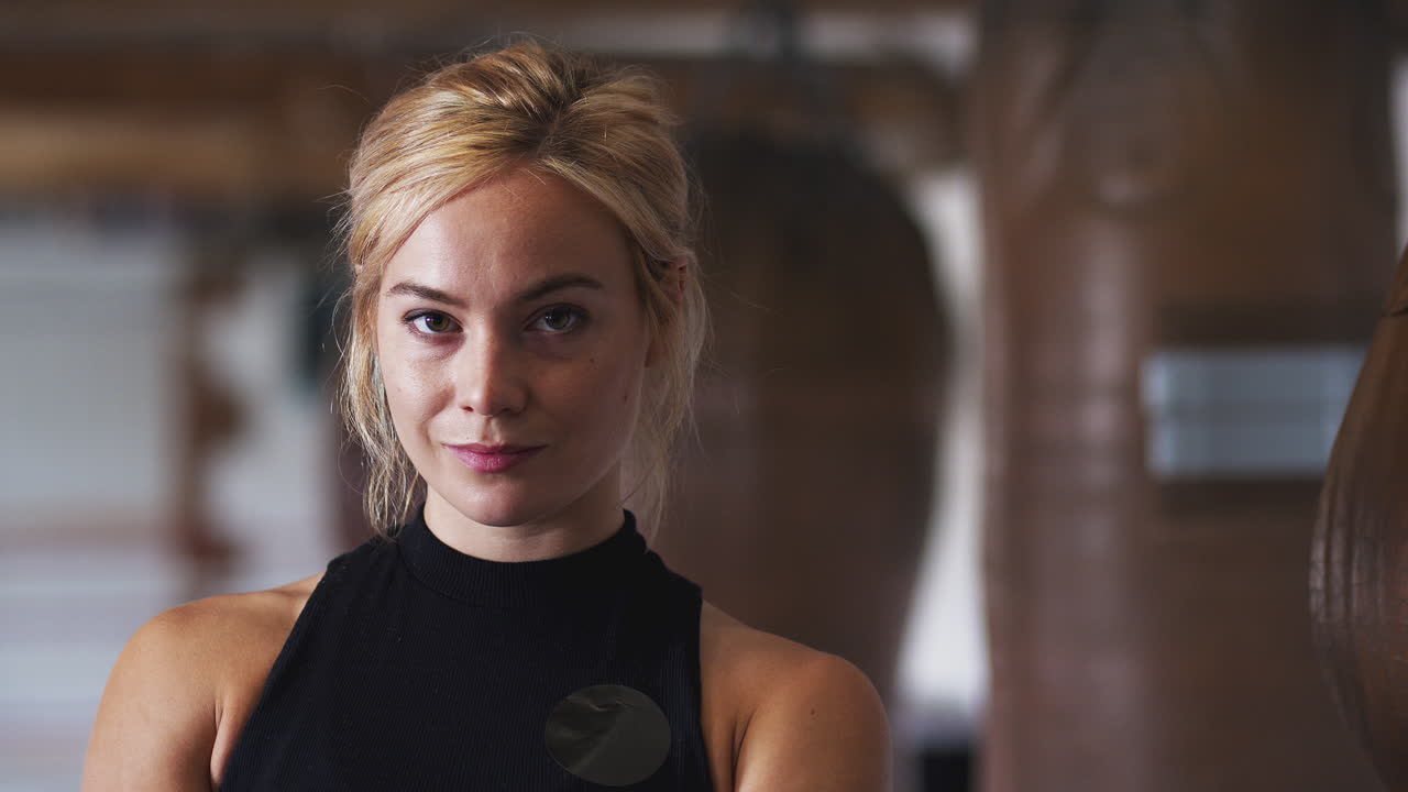 Portræt af kvindelig bokser, der træner med gammeldags sandsække i fitnesscenteret.