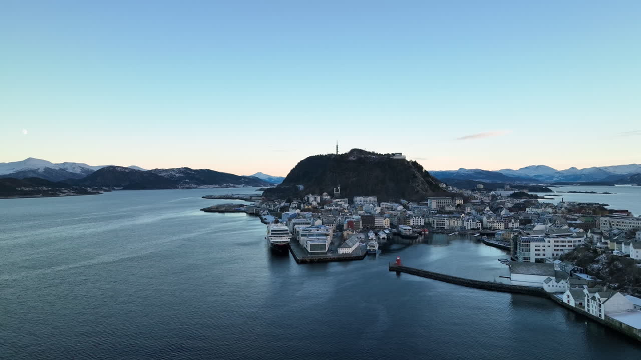 Norway 4K Aerial of &Aring;lesund in winter slowly descending looking back at the harbour with beautiful sunset in the background
