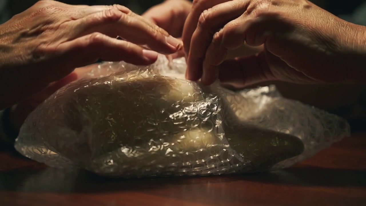Feeling bubble wrap, two pairs of hands peeling bubble wrap on wooden table, inspecting pale object