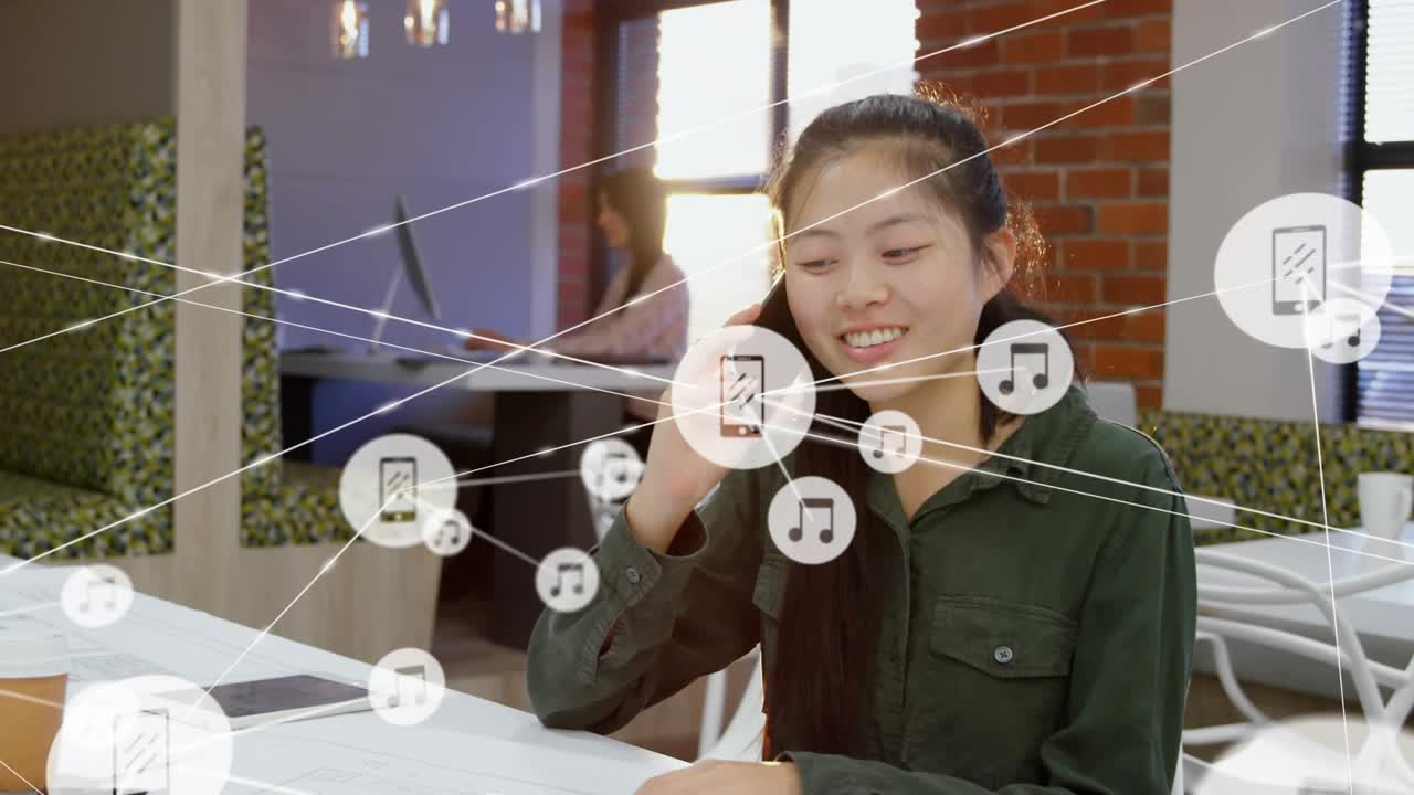 Seated woman tapping phone and calling, causing animated icons growing across coworking space table