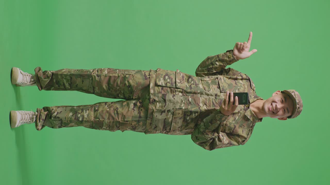 Full Body Of Asian Man Soldier Using Smartphone And Pointing To Side While Standing In The Green Screen Background Studio
