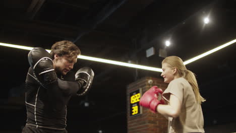 Friendly-fit-girl-training-with-coach-on-boxing-ring.-Female-boxer-boxing-at-gym