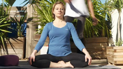a yogi applies a singing bowl behind a woman meditating during a yoga session