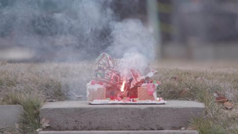 a christmas ginger bread and graham cracker house or decoration has a large fire cracker or m 80 being lit on it by a flame from a blow torch