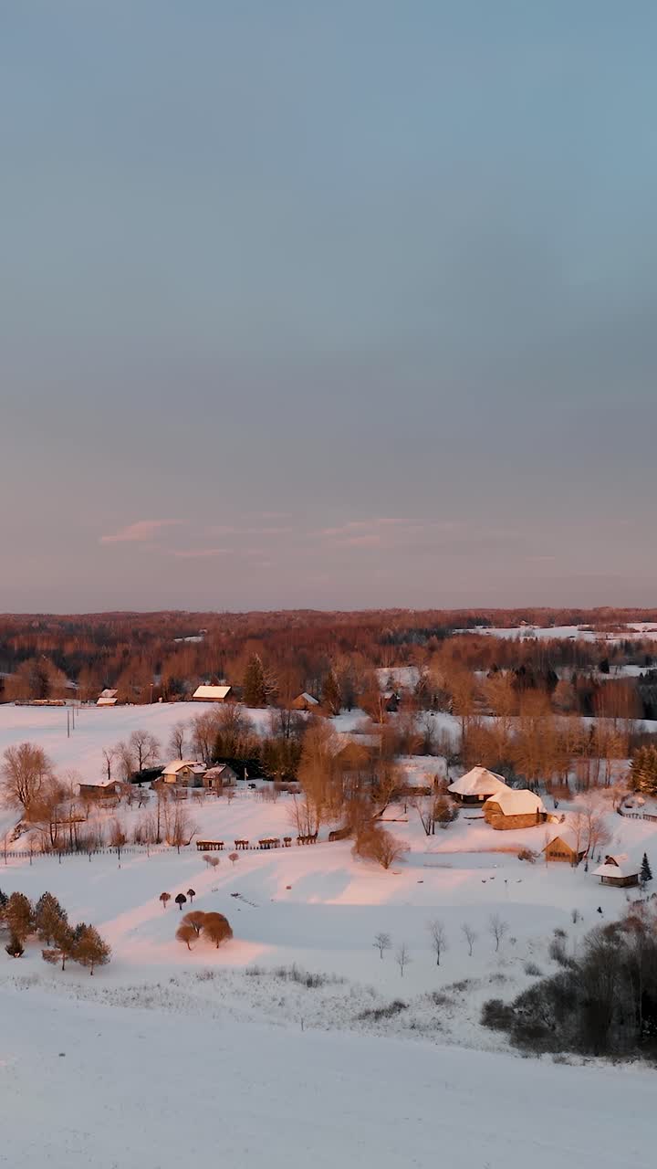 Vertical aerial view of a household community in the countryside during winter with lots of snow. Multiple family houses in suburbs at vibrant sunset.