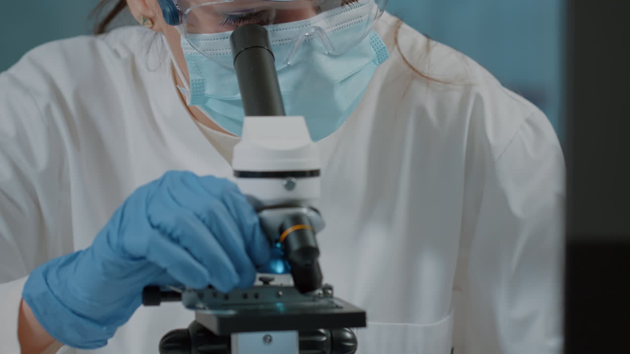 Biologist with face mask using microscope to work on experiment