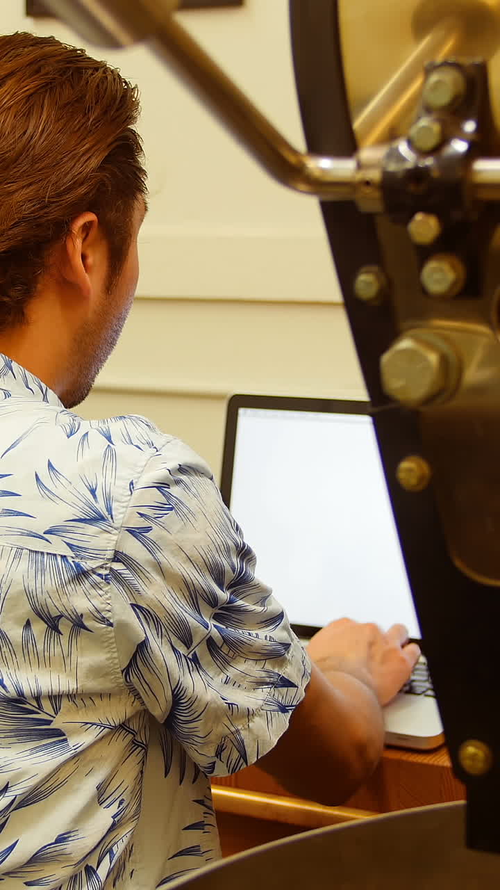 hombre usando una computadora portátil mientras está sentado al lado de la máquina de tostado de café