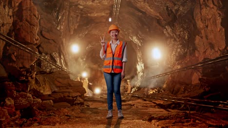 full body of asian female engineer with safety helmet smiling and showing peace gesture in underground mine tunnel