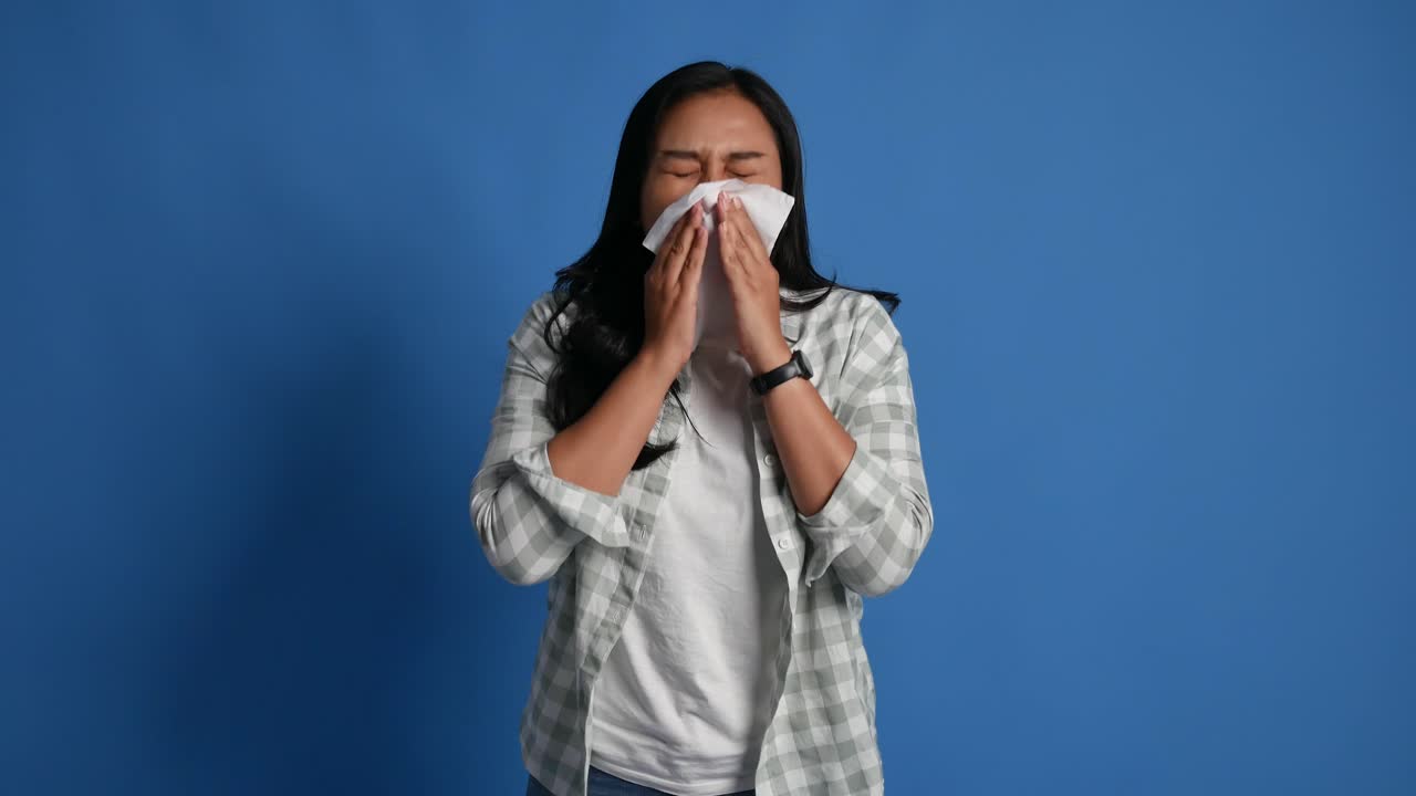 A young asian woman suffers from acute respiratory viral infections and blows her nose on a napkin against an isolated background