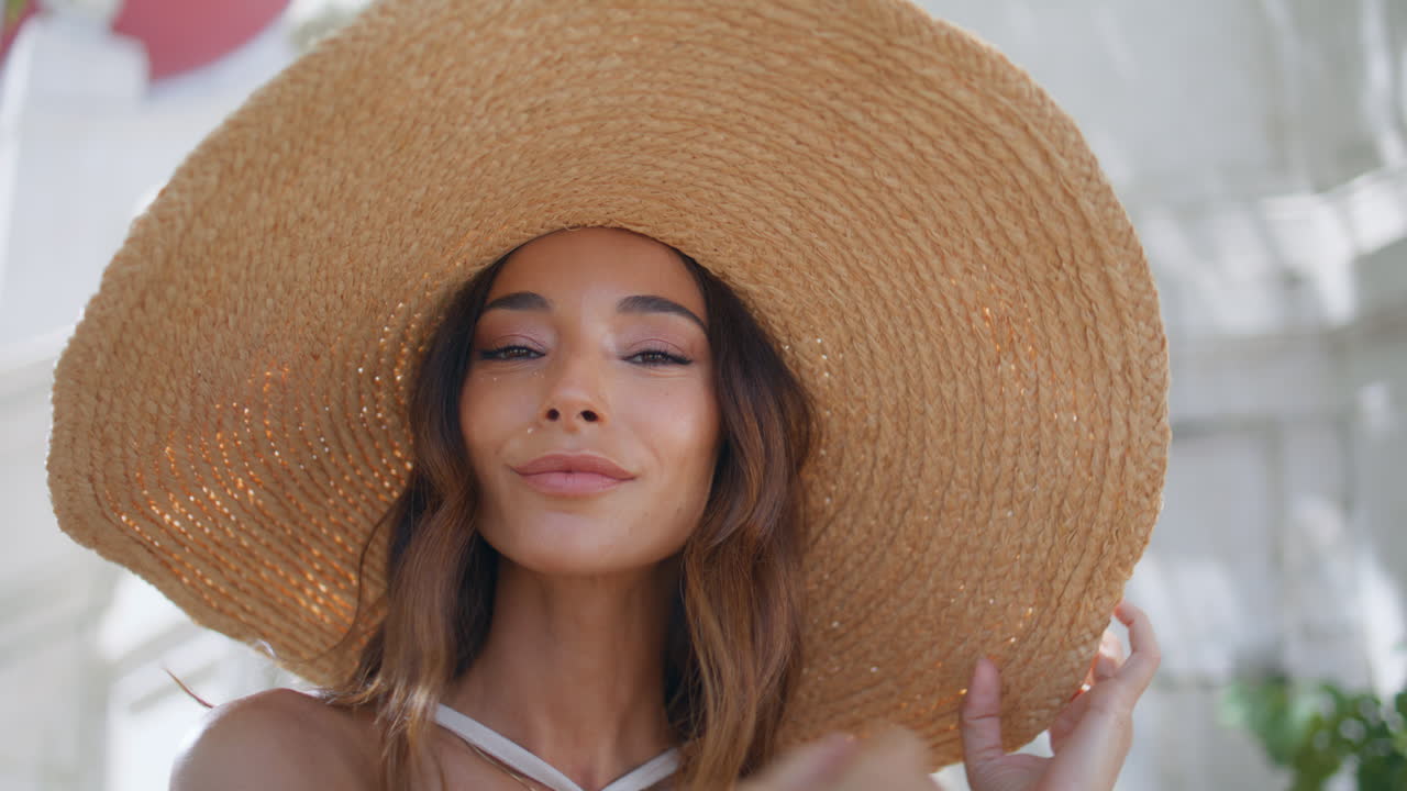 Ritratto di ragazza con cappello di paglia in posa in città con volto sorridente. La modella guarda la fotocamera.