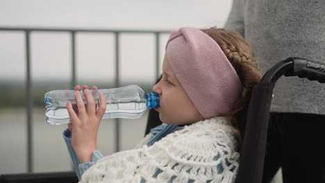 Das-Durstige-Mädchen-Trinkt-Wasser-Und-Sitzt-Im-Rollstuhl-Neben-Der-Mutter