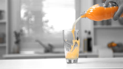 mans hand pouring orange juice from a bottle into a glass