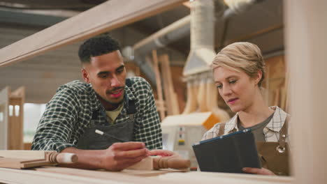 aprendices masculinos y femeninos con tabletas digitales trabajando como carpinteros en un taller de muebles