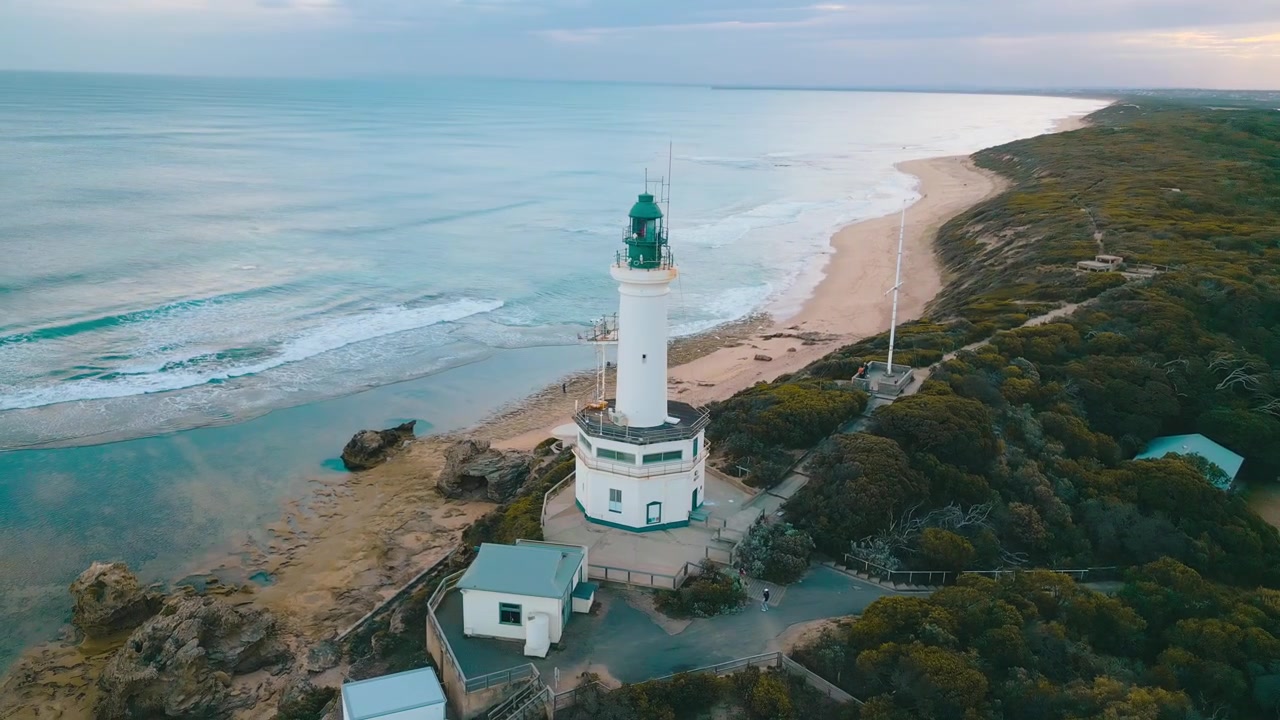 Betagende filmisk 4K luftdroneoptagelse med Point Lonsdale Fyr, mole ved vandet og vidtstrakte havudsigter under klar aftenhimmel.