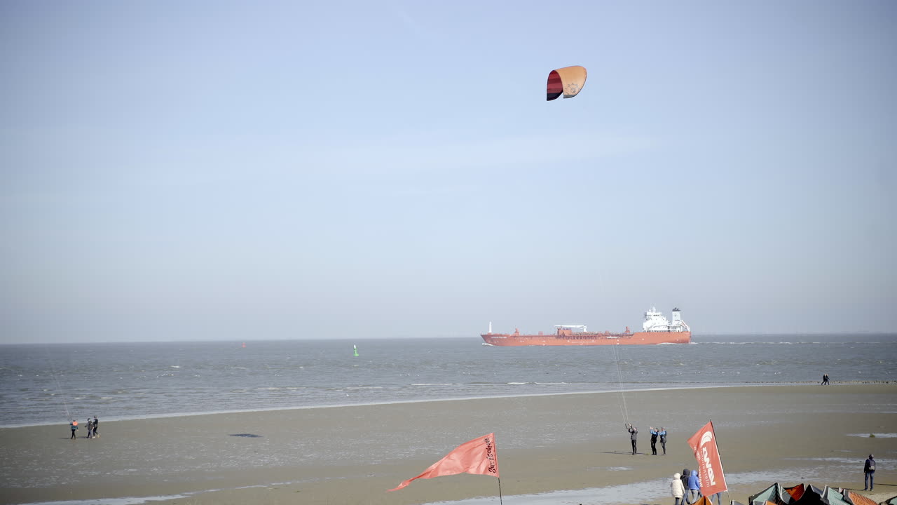 Wadden sea kite surfing and passengers or people on the beach with big red ship on water 4K