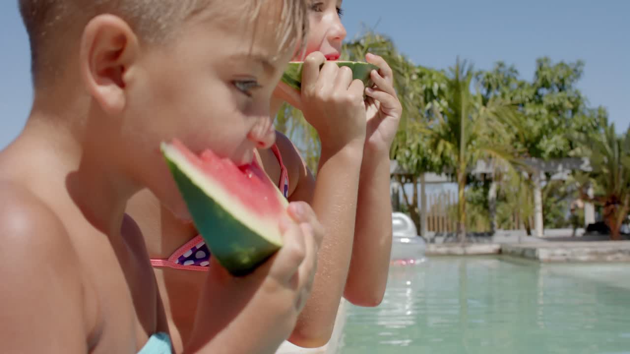Felices hermanos caucásicos comiendo sandía en la piscina de una casa de playa.