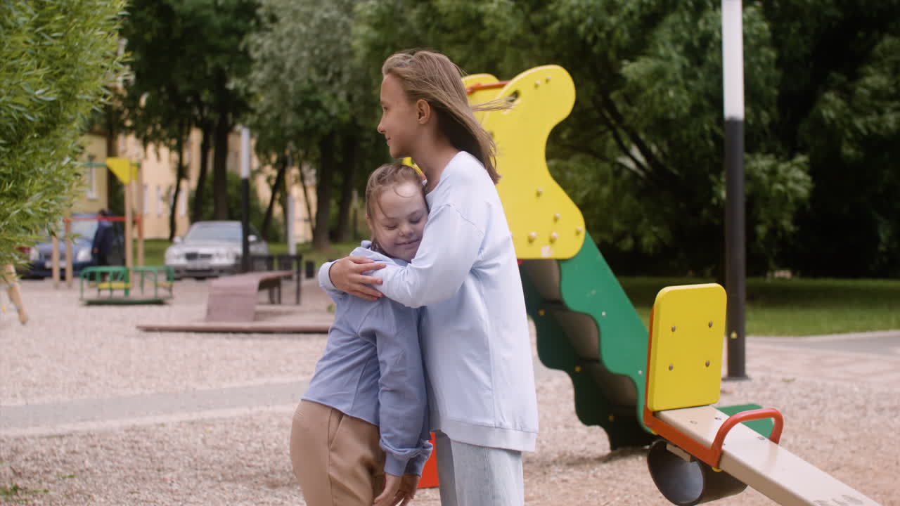 Little girl with down syndrome hugging another girl in the park on a windy day