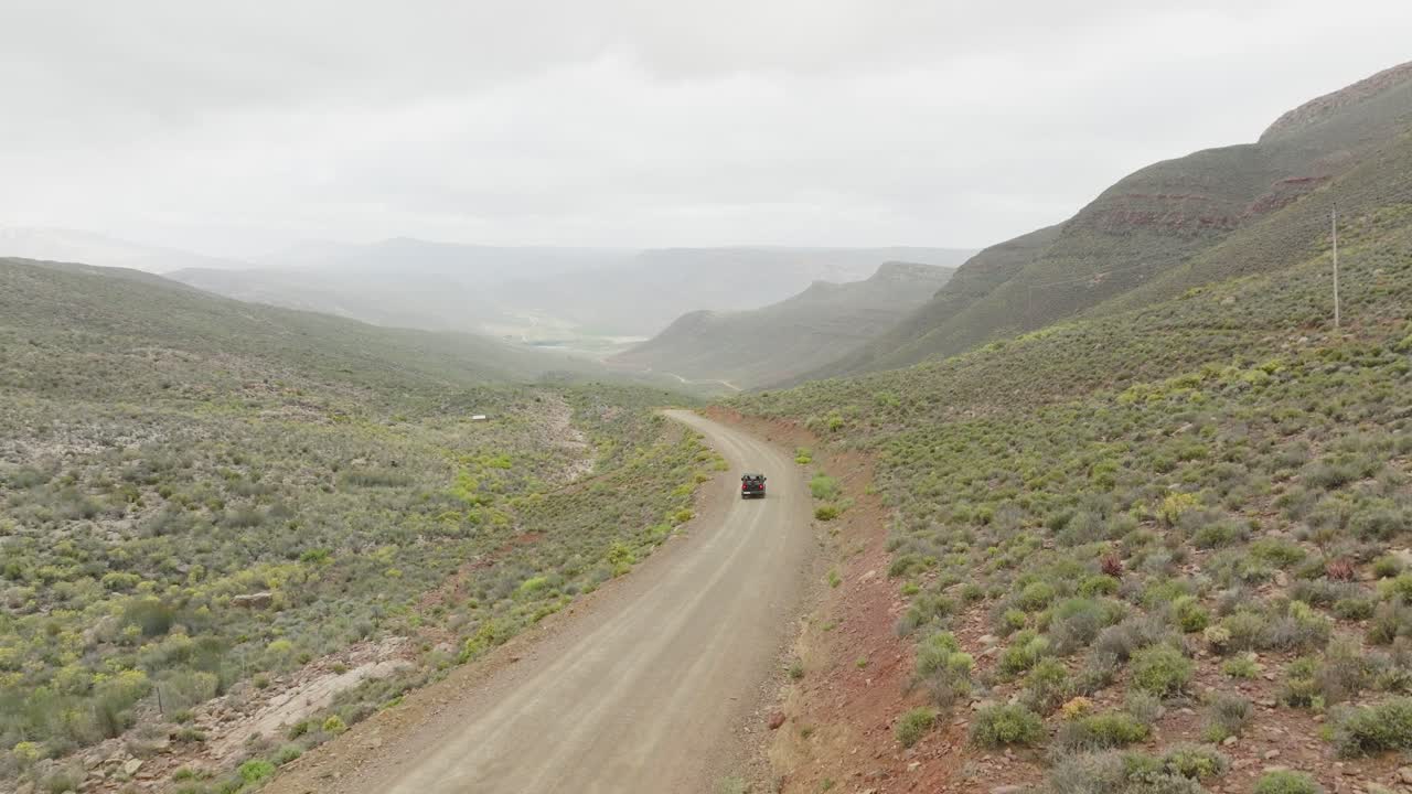 드론이 서서히 길 으로 올라가서 검은색 오프 로드 차량이 남아프리카 공화국의 세더버그 야생 지역에서 운전하는 곳 - 배경에는 바위 산을 볼 수 있습니다.