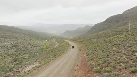 el avión no tripulado sube lentamente hacia arriba junto a una carretera donde un vehículo fuera de carretera negro conduce en el área silvestre de cederberg en sudáfrica - en el fondo se pueden ver montañas rocosas