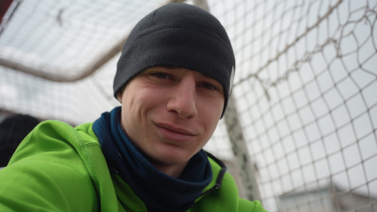 골키퍼가 멋지게 선방한 후 미소를 짓고, 골대 옆에서 팀 동료와 함께 은은하게 기뻐하는 모습, 기쁨과 안도감이 느껴지는 솔직한 표정, 추운 날씨, 진정한 스포츠맨십을 가까이에서 포착