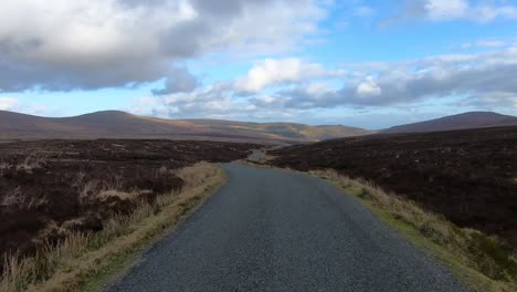 POV-shot,-Point-of-view-through-a-windshield-as-driving-on-a-beautiful-scenery-with-hills,-blue-sky-and-clouds