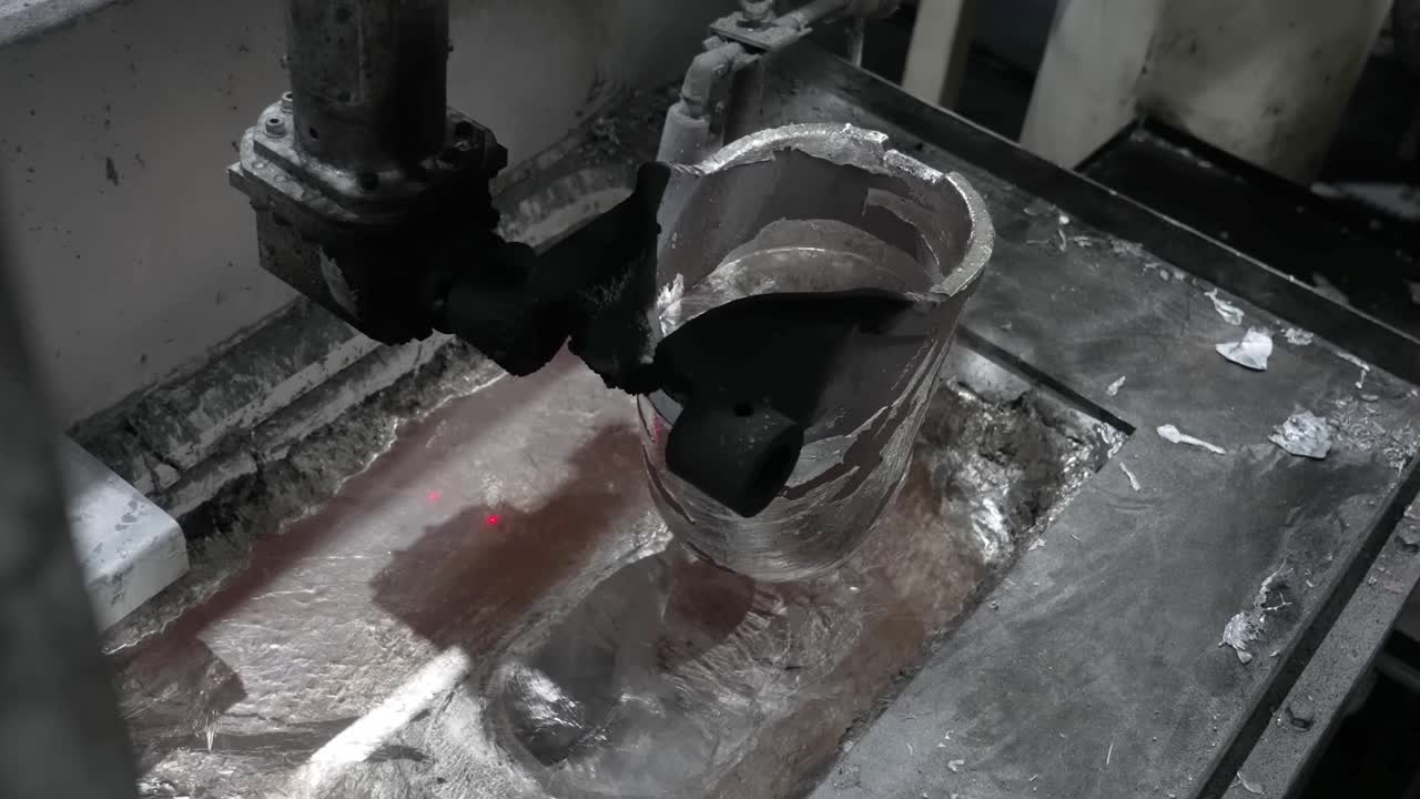 Braccio robotico che solleva una siviera piena di alluminio fuso incandescente da un forno durante un'operazione di colata ad alta velocità