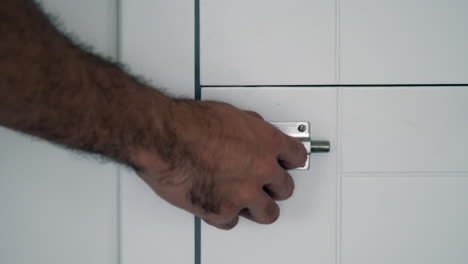 garantizar la privacidad: primer plano de la mano que encierra el cerrojo de la puerta del baño moderno