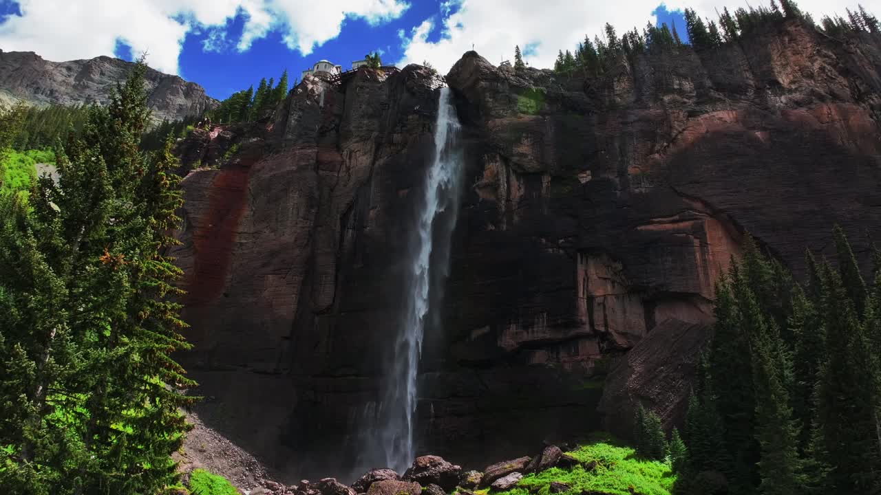Telluride Bridal Veil Falls aerial drone Waterfall Telluride windy mist spray Black Bear Pass Road Colorado pine tree Ouray Ridgway Box Canyon cliffside 4wd hiking cloudy sun blue sky upwards jib