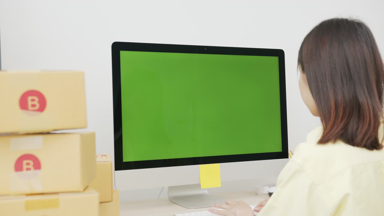 pequeña empresa de puesta en marcha, joven mujer asiática comprobando el pedido en línea en la computadora con pantalla verde. y embalaje de cajas para productos para enviar a los clientes.