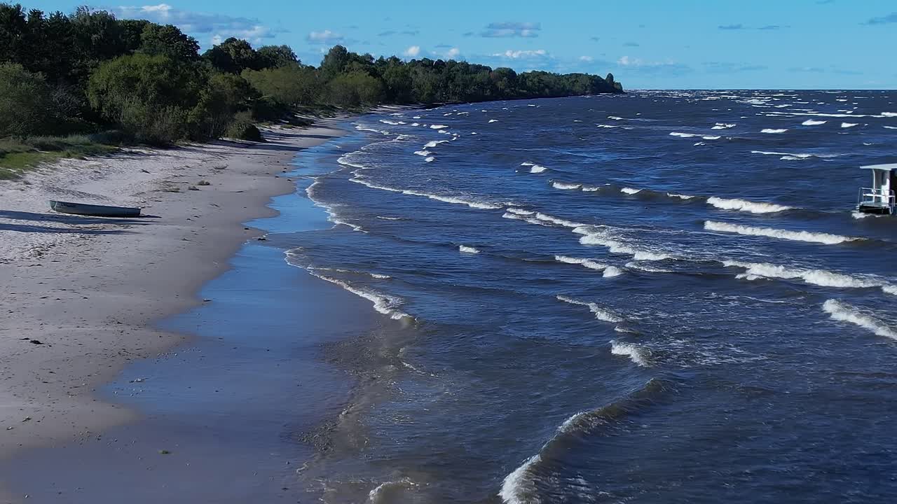 Wellen spülen an der Ostsee an Land, nahe einem Sandstrand, der mit Booten übersät ist.