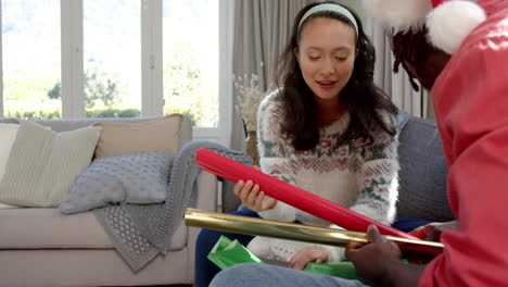 happy diverse couple sitting on couch choosing christmas wrapping paper, copy space, slow motion