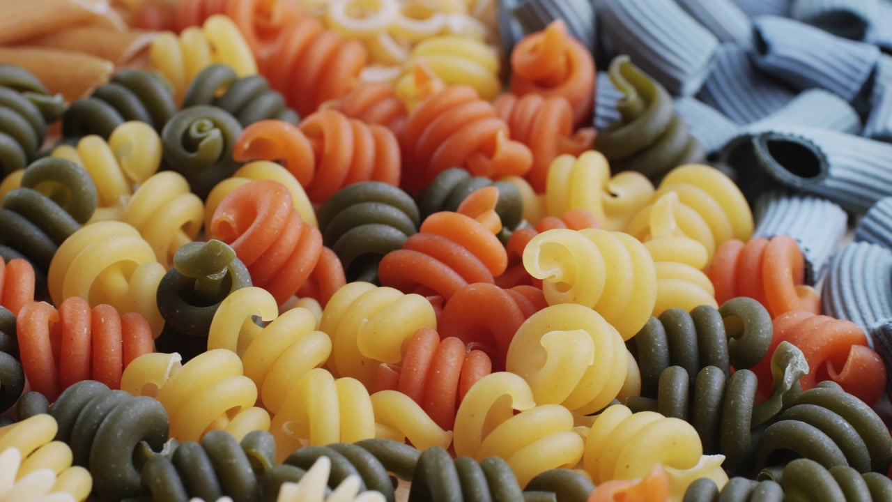 Close-Up Pan of Various Uncooked Colorful Pasta Shapes