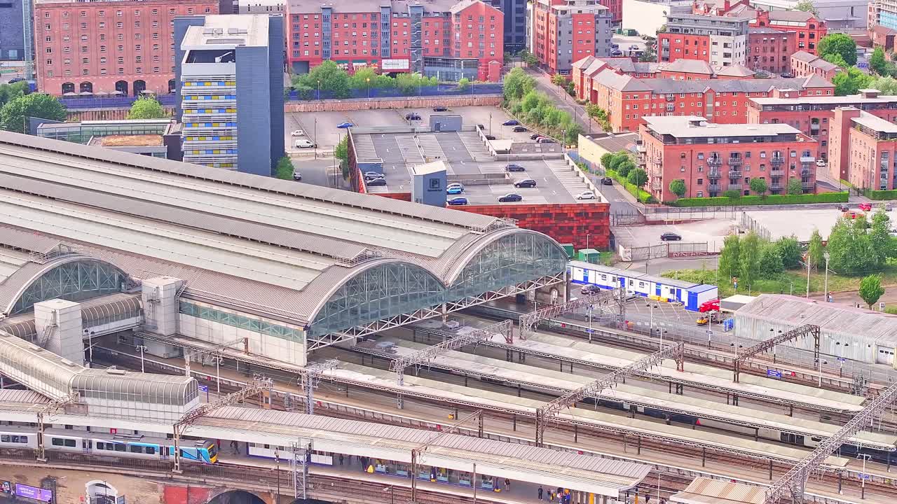 Aerial static shot of Manchester Piccadilly Station in Manchester, England, showing platforms, trains, brick buildings and curved glass roof structure surrounded by urban infrastructure and traffic