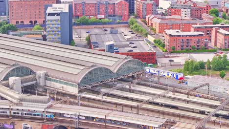 aerial static shot of manchester piccadilly station in manchester, england, showing platforms, trains, brick buildings and curved glass roof structure surrounded by urban infrastructure and traffic